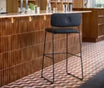 Bla Station Dundra Bar Chair in a café bar setting with a black steel frame and dark upholstered seat and backrest.