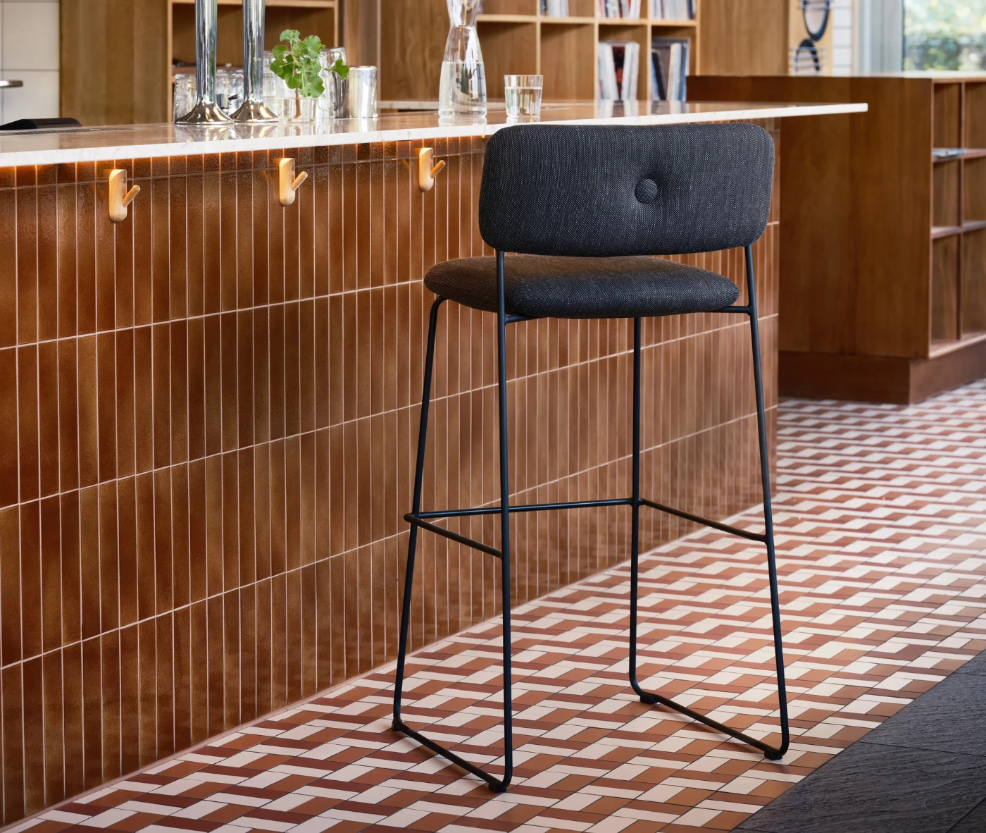 Bla Station Dundra Bar Chair in a café bar setting with a black steel frame and dark upholstered seat and backrest.