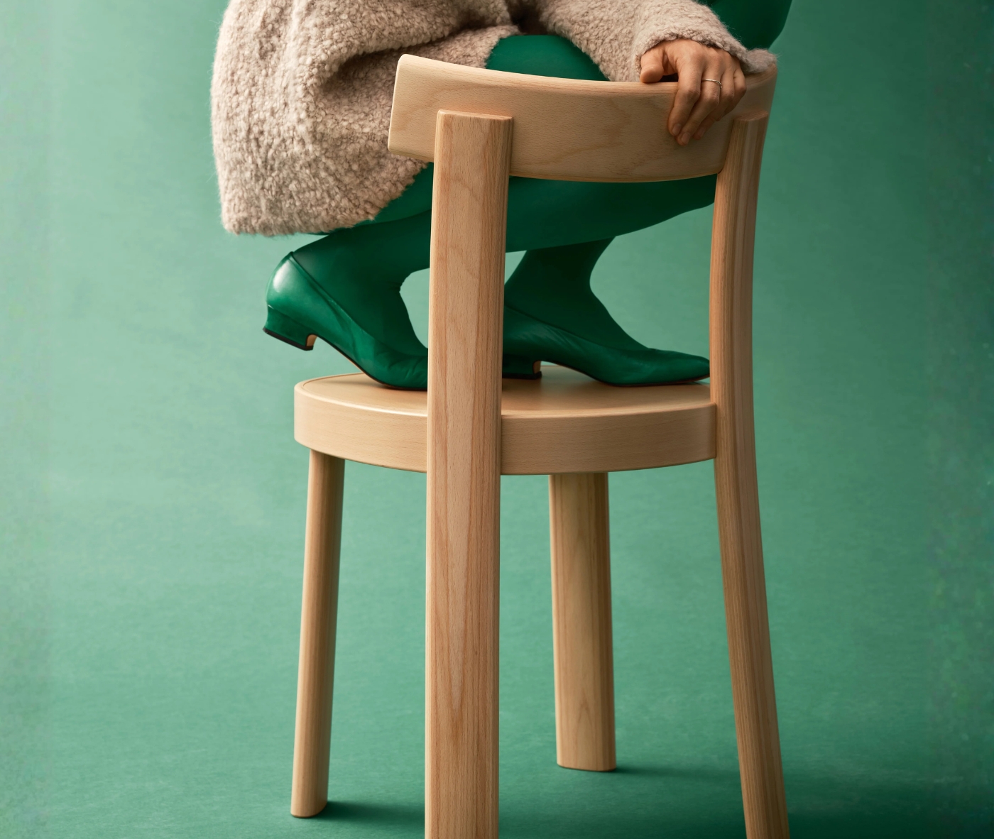 Person seated on a Bla Station Frankfurter chair in natural timber finish, shown in a studio setting.