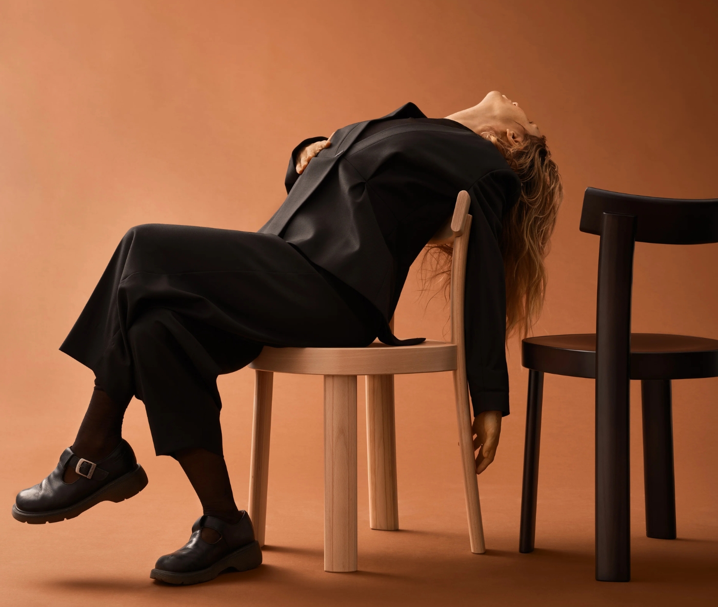 Bla Station Frankfurter chairs in natural and black timber finishes, with a person reclining on the natural timber chair in a studio setting.