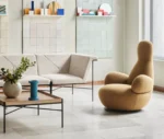 Bla Station Oppo lounge chair in a lounge setting with fully upholstered mustard yellow fabric and a high rounded back.