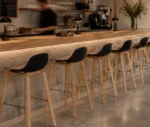 P4 Loop Mini stools lined up in hospitality setting with backrests and natural timber legs.