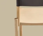 Detail view of True Adinne in studio setting with light timber frame and black leather backrest.