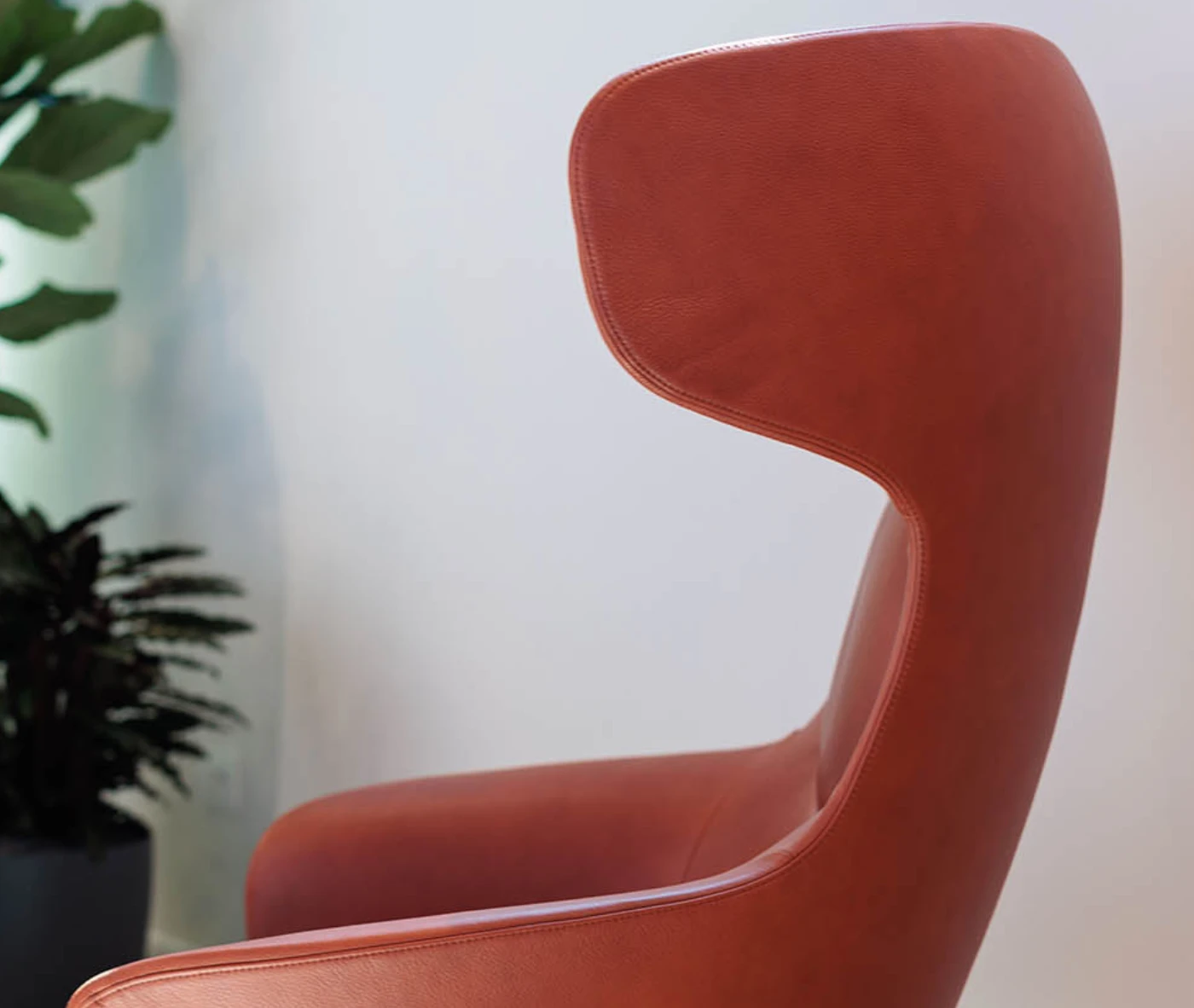 Close-up in side view of True Ahkka lounge chair with curved upholstered shell and headrest.