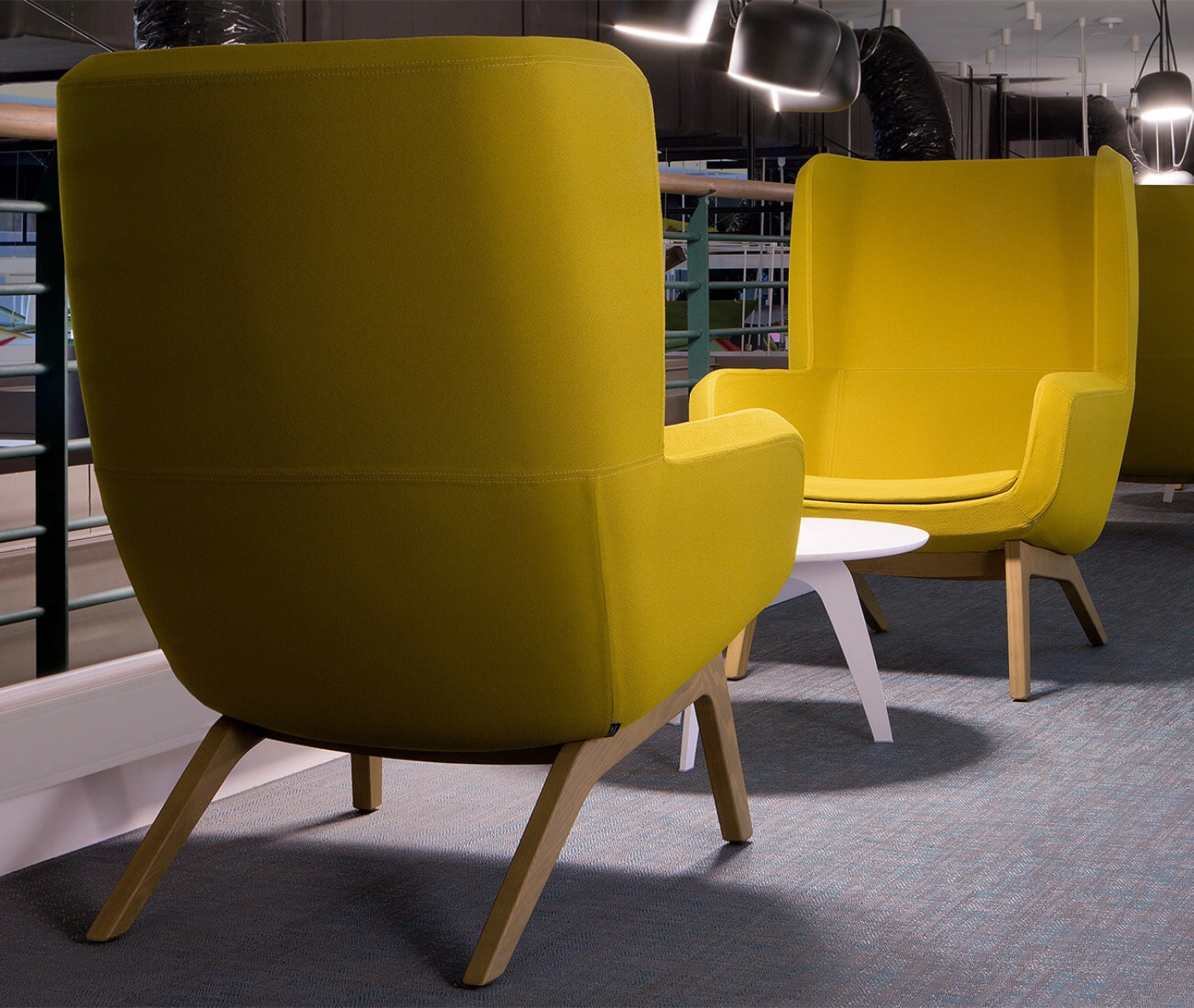 True Arca high-back lounge chair in an office setting with high yellow upholstered backrest, seat pad, and timber legs.