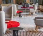 True Arca high-back chair in a lobby setting with high grey upholstered backrest, seat pad, and timber legs.