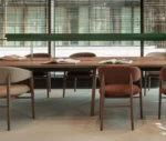 True Aura chair surrounding Wing table, with an upholstered seat and backrest with solid timber legs.