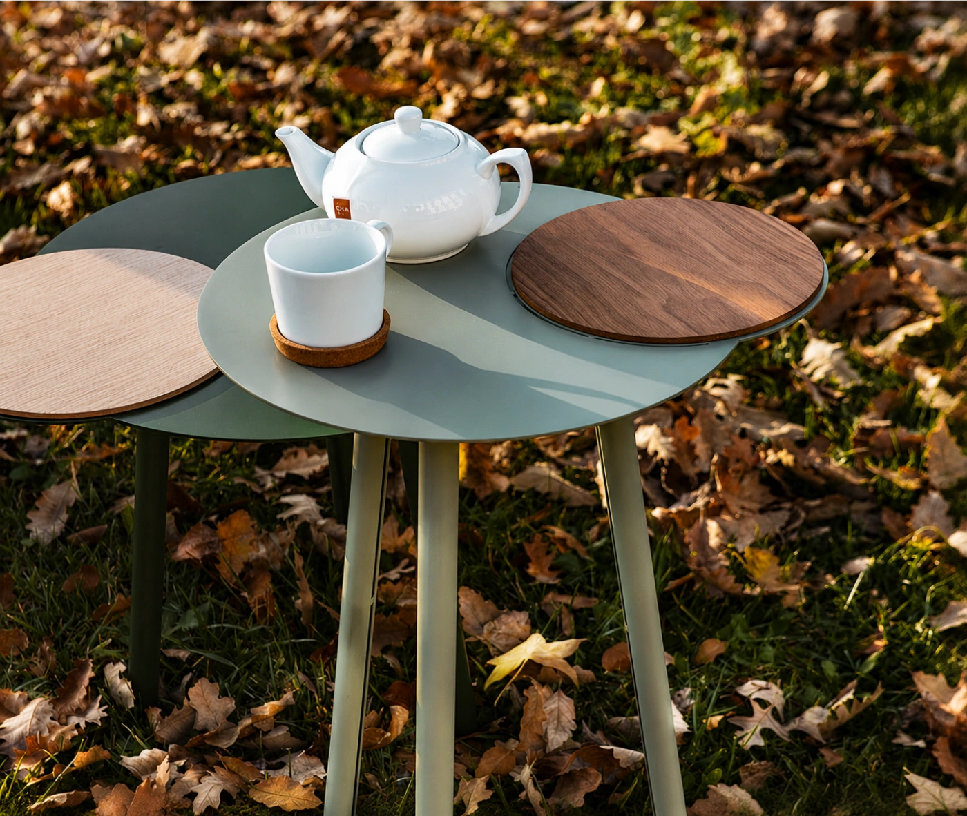 True Cloud round table with light and dark green finish and removable timber tray in an outdoor setting.