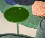 Close-up of the True Cremino table in a showroom setting, with a green glass tabletop.