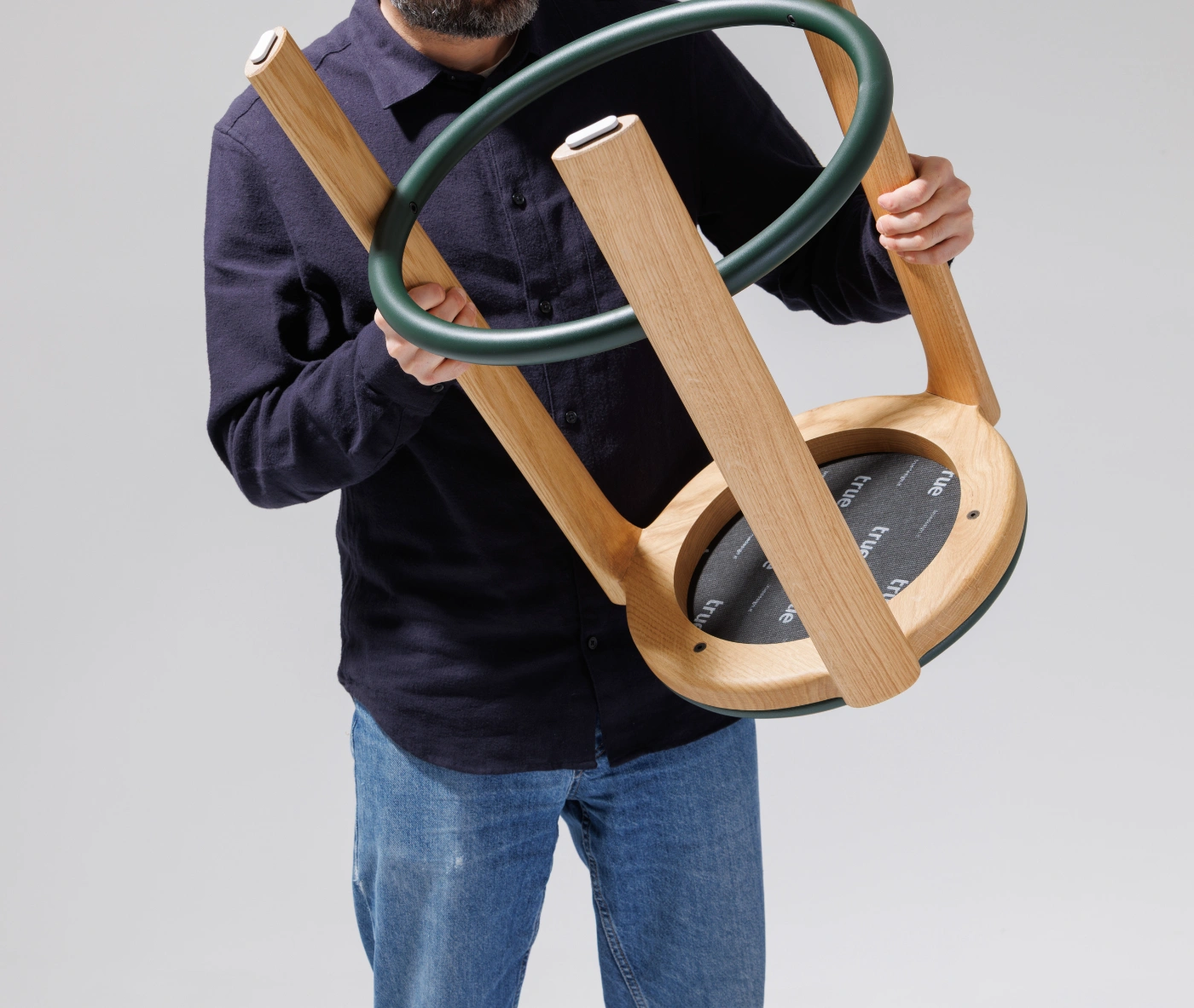 True Cute stool held upside down by a person, showing its timber frame and circular footrest.