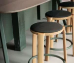 True Cute stools with dark upholstered seats, timber legs, circular footrests in a hospitality setting.