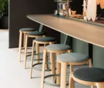 True Cute stools with dark upholstered seats, timber legs, circular footrests in a hospitality setting.