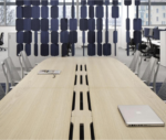 True Wing table in a workplace setting with a light timber tabletop, timber legs, and an integrated magnetic beam for cable management.