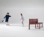 Urbantime Liberty.080 curved outdoor bench shown in a studio setting with children playing.