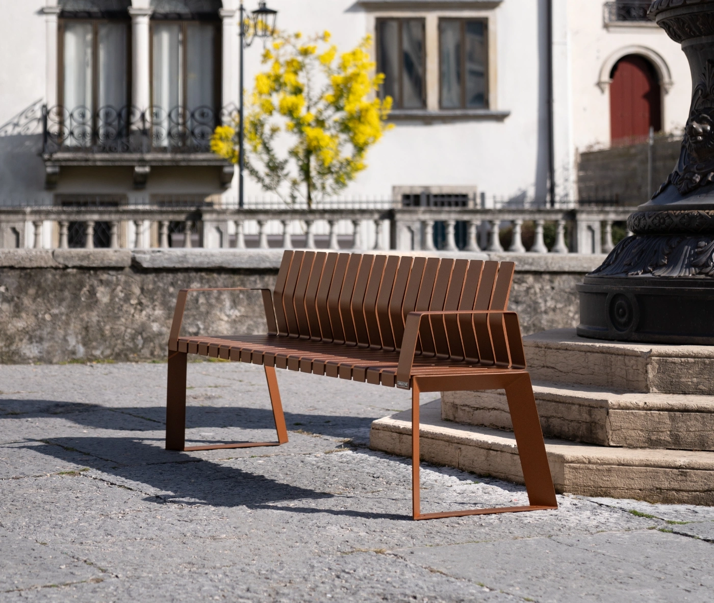 Urbantime Liberty.080 outdoor slat bench in front-left view set in an urban plaza.