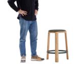 True Cute stool with a dark leather upholstered seat, timber legs, circular footrest and a person seated on it.