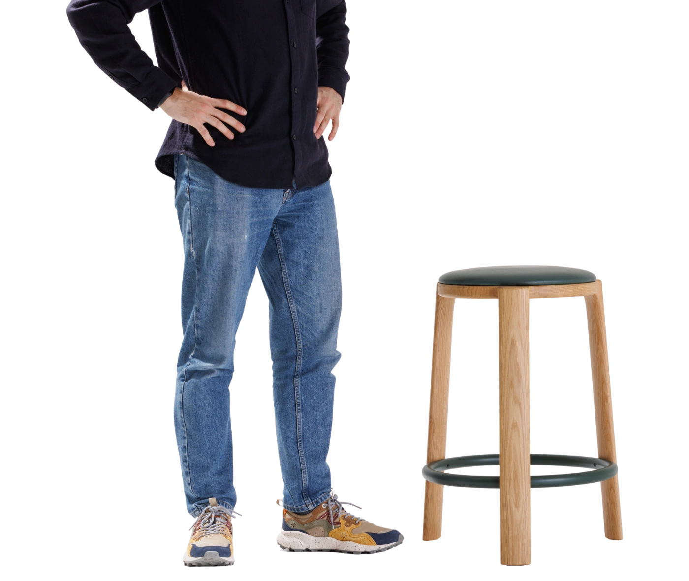 True Cute stool with a dark leather upholstered seat, timber legs, circular footrest and a person seated on it.