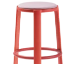Close-up of True Cute stool with a light pink upholstered seat, long red timber legs and a circular footrest.